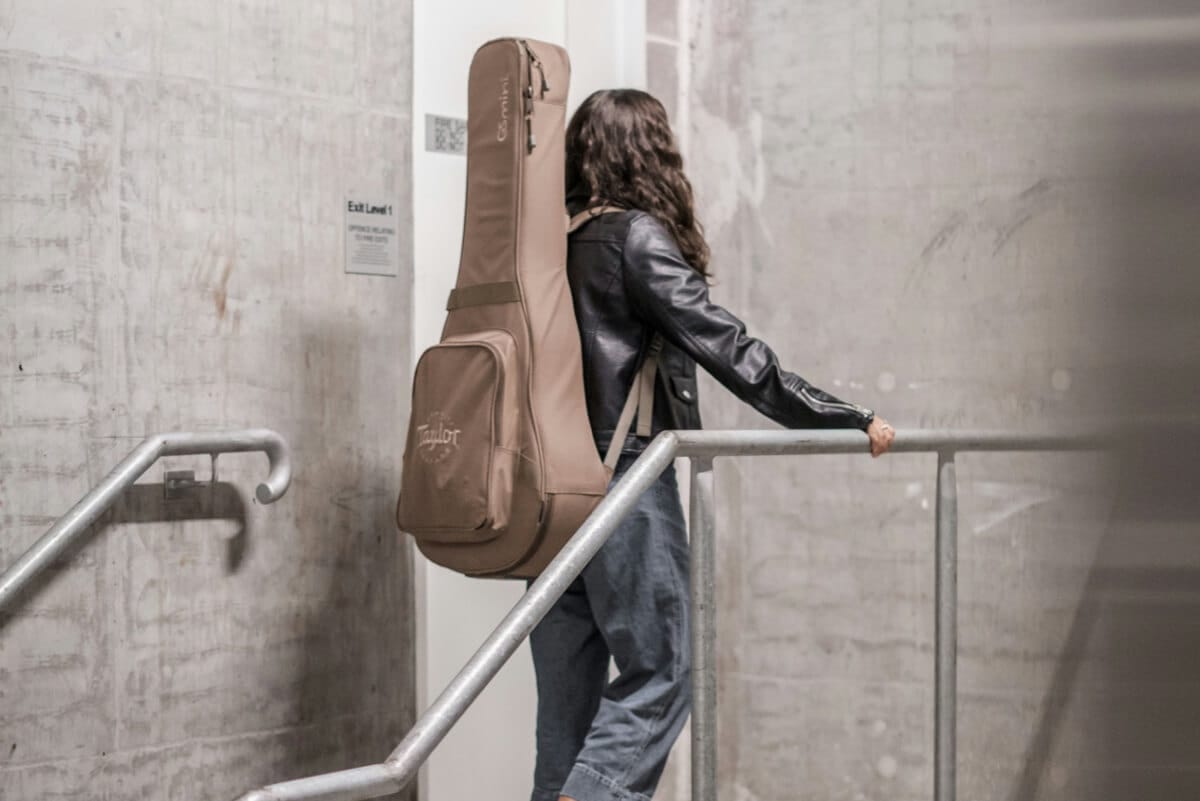 Young woman approaching an internal door in a building, with a guitar case strapped to her back