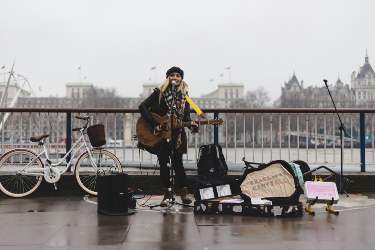 Photo of a young female singer with a guitar, performing on a bridge in the rain