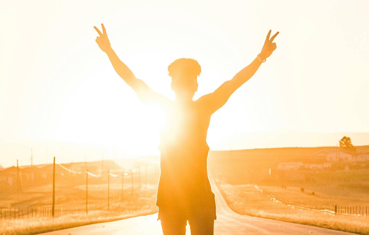 Young person with hands with victory signs, lit by sunlight